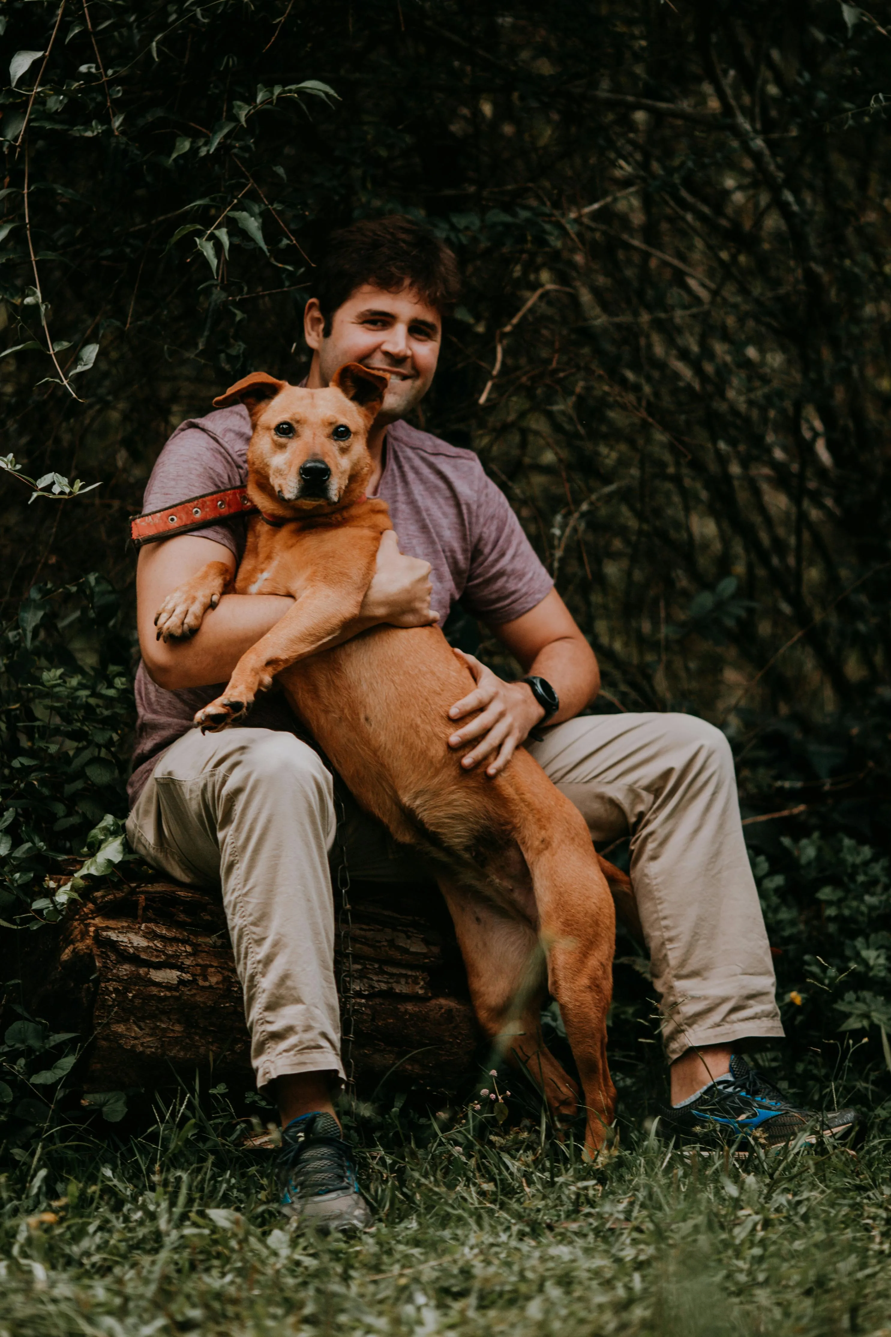 a pet worker sitting outside smiling with a dog
